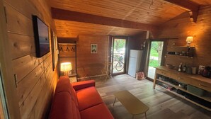 Ein Holzinnenraum mit einem roten Sofa, einem kleinen Tisch, einem Fernseher und einer Küchenzeile mit Regalen.
