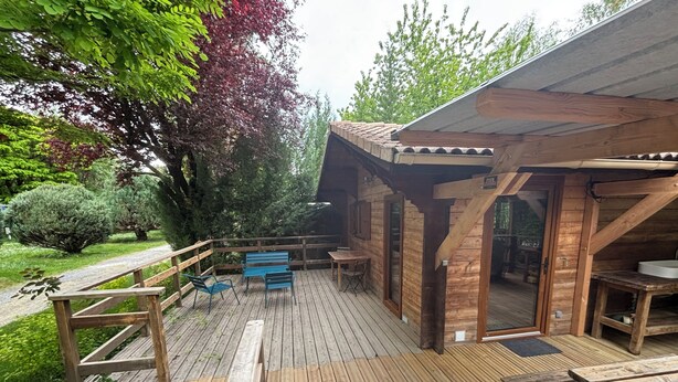 Eine Holzterrasse mit Sitzgelegenheiten im Freien, einem überdachten Bereich und Blick auf die umliegende Natur.