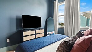 A bedroom with a bed, a television, a dresser, and a window with curtains.