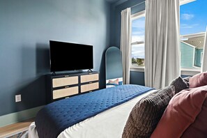 A bedroom with a bed, a television, a dresser, and a window with curtains.