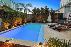A swimming pool with a tiled deck, surrounded by a wooden fence and various plants. - Maison de Toulouse | Moody | Heated Pool • Near FQ (New Orleans)