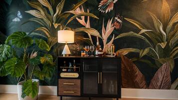 A room with a dark-themed mural, a black cabinet with drawers, a table lamp, and a potted plant.