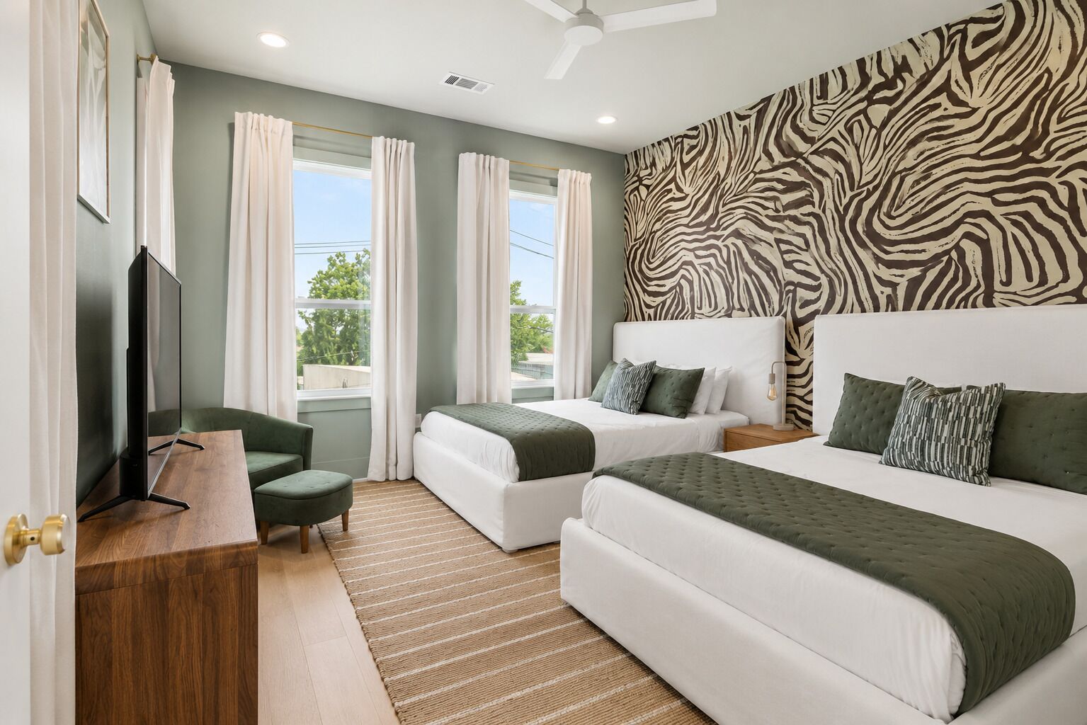 A hotel room with two beds, a TV, a desk, and a zebra-patterned wall.