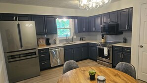 Une cuisine moderne avec des meubles de couleur sombre, des appareils électroménagers en acier inoxydable, une table à manger en bois et un lustre.