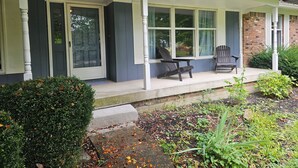 Une maison avec un porche, deux chaises et une petite table.