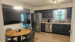 Une cuisine moderne avec des meubles de couleur sombre, des appareils en acier inoxydable, une table à manger en bois et une grande fenêtre.