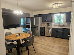 A modern kitchen with dark cabinets, stainless steel appliances, a wooden dining table, and a large window. - 3 Bedroom Grand Park Retreat in Westfield, IN (Westfield)