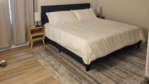 Une chambre à coucher avec un lit, une table de chevet, une lampe, un plancher en bois et un tapis à motifs.