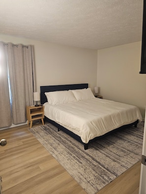 A bedroom with a bed, a nightstand, a lamp, a wooden floor, and a patterned rug. - 3 Bedroom Grand Park Retreat in Westfield, IN (Westfield)