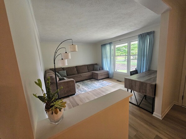 A living room with a sofa, a dining table, a plant, and a window with curtains. - 3 Bedroom Grand Park Retreat in Westfield, IN (Westfield)