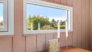 A room with wooden walls, a large window with a view of greenery, a wooden table, and a candle holder.