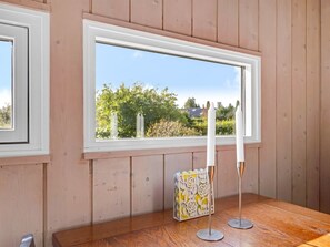 A room with wooden walls, a large window with a view of greenery, a wooden table, and a candle holder. - "Söhnke" - 100m to the fjord by Interhome (Faxe)