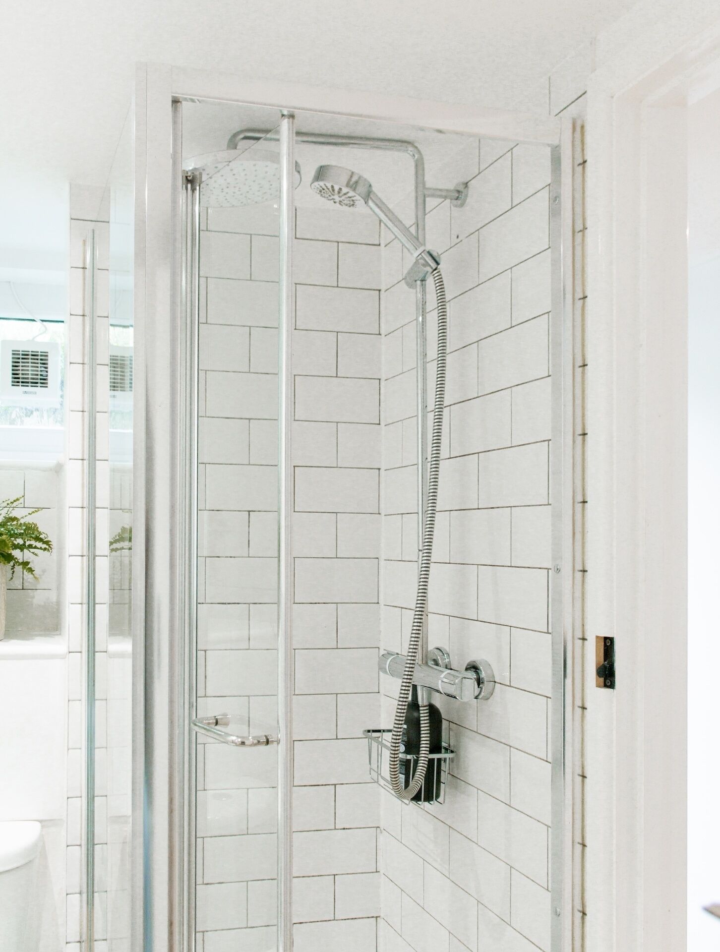 Ducha con cerramiento de vidrio, cabezal de ducha de mano y grifo de pared.