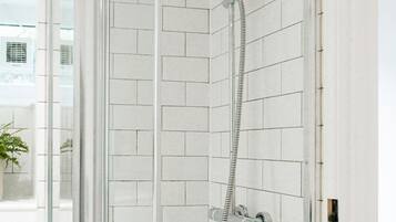 Ducha con cerramiento de vidrio, cabezal de ducha de mano y grifo de pared.
