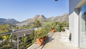 Un balcon agrémenté de plantes en pot, doté d’une rambarde en métal, et offrant une vue sur les montagnes et une ville.