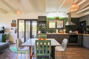 A modern kitchen with a dining area, featuring a large island, pendant lighting, and a view through the sliding doors.