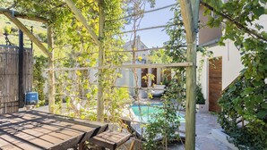 Une pergola en bois ornée de plantes grimpantes, une piscine en pierre et une table de patio.