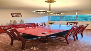Un coin repas avec une table rouge, des chaises en bois, un lustre et une fenêtre donnant sur un beau paysage.