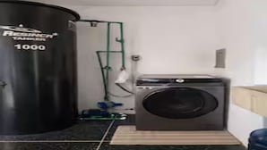Une pièce contenant un grand réservoir noir portant l’inscription « Réservoir Resinco 1000 », un lave-linge et un tuyau d’arrosage vert.