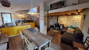 A cozy interior with a wooden dining table, yellow kitchen counter, and a stone wall.