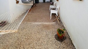 Une petite cour étroite avec un hamac, des chaises blanches, des plantes en pot et une petite table.