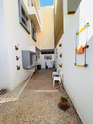 A narrow courtyard with a hammock, white chairs, potted plants, and a small table. - Aji darna -cozy morrocan stay in fes (Fes)