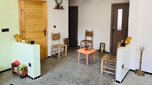 Une pièce avec une porte en bois, deux chaises en osier, une petite table, un luminaire suspendu et une horloge murale.