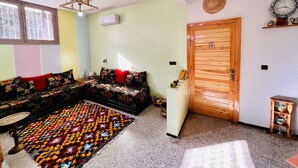 Un salon avec un canapé, un tapis à motifs, une porte en bois et une horloge fixée au mur.