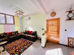 A living room with a sofa, a patterned rug, a wooden door, and a wall-mounted clock. - Aji darna -cozy morrocan stay in fes (Fes)