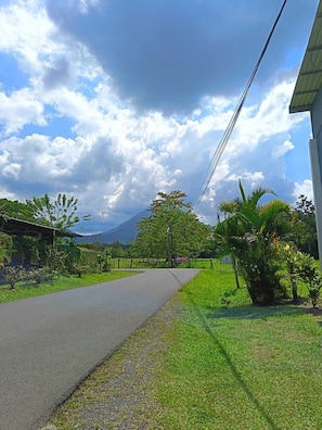 A paved road with grass on either side, trees, and a mountain in the distance. - Apartment in La Fortuna 2 min from the park (La Fortuna)
