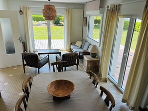 A dining area with a large wooden table, chairs, a sofa, and a lamp. - Les Lutins - Family home - Private beach access (Concarneau)