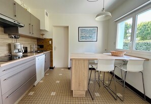 A modern kitchen with a wooden countertop, white chairs, a dining table, and a window with a view of trees. - Les Lutins - Family home - Private beach access (Concarneau)