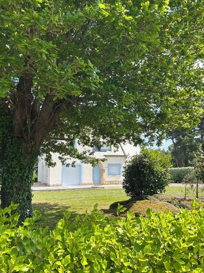 A building with a blue door and a stone wall, surrounded by greenery. - Les Lutins - Family home - Private beach access (Concarneau)