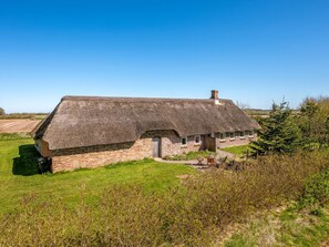 A thatched-roof house with a brick exterior, surrounded by a grassy field and trees. - "Petteri" - 600m to the fjord by Interhome (Tim)