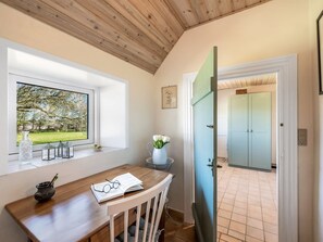 A room with a wooden ceiling, a window with a view of a garden, a door leading to another room, and a table with a book and glasses. - "Petteri" - 600m to the fjord by Interhome (Tim)
