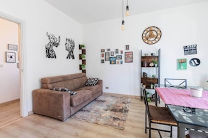 Een woonkamer met een bruine bank, een salontafel, een vloerkleed en wanddecoraties, waaronder ingelijste foto’s en een klok.