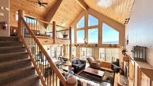 A spacious interior with a wooden staircase, a living area with a sofa and coffee table, and large windows offering a view.