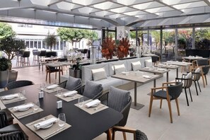 A modern outdoor dining area with tables and chairs, a sofa, and potted plants. - Premium 1BR living |Comfort & Class + City Center (Dubai)