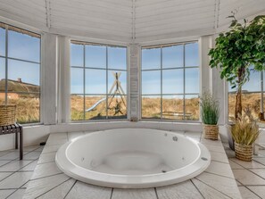 A spa room with a large bathtub, three windows with a view of a landscape, and a potted plant. - "Riika" -  from the sea by Interhome (Ringkøbing)