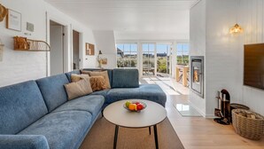 En moderne stue med en blå sofa, et rundt sofabord med frugt, og en pejs.