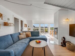En moderne stue med en blå sofa, et rundt sofabord med frugt, og en pejs.