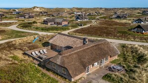Et stråtækt hus med terrasse, omgivet af et landligt landskab.