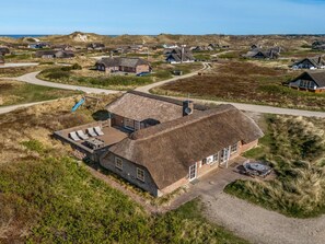 Et stråtækt hus med terrasse, omgivet af et landligt landskab.