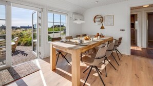 Et spiseområde med et træbord, stole og udsigt gennem store vinduer.