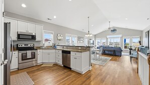 A modern kitchen with white cabinetry, stainless steel appliances, and a large island. - Salt Life | Deck Views + Steps to Beach, Sleeps 10 (North Topsail Beach)