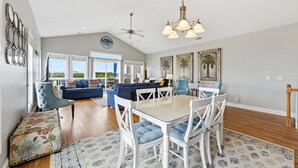 A spacious living area with a dining table, blue upholstered furniture, and a ceiling fan. - Salt Life | Deck Views + Steps to Beach, Sleeps 10 (North Topsail Beach)