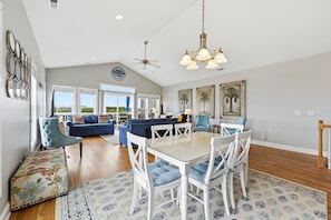 A spacious living area with a dining table, blue upholstered furniture, and a ceiling fan. - Salt Life | Deck Views + Steps to Beach, Sleeps 10 (North Topsail Beach)