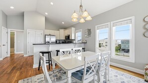 A modern kitchen with white cabinets, a dining table with chairs, and a chandelier. - Salt Life | Deck Views + Steps to Beach, Sleeps 10 (North Topsail Beach)