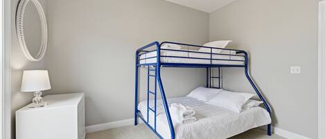 A bunk bed with a white mattress and pillows, a white bedside table with a lamp, and a wall-mounted mirror.