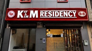 Un edificio con fachada roja y gris, con la señalización 'KAY & M RESIDENCY' y 'B&B', que indica que se trata de un hospedaje tipo bed and breakfast.